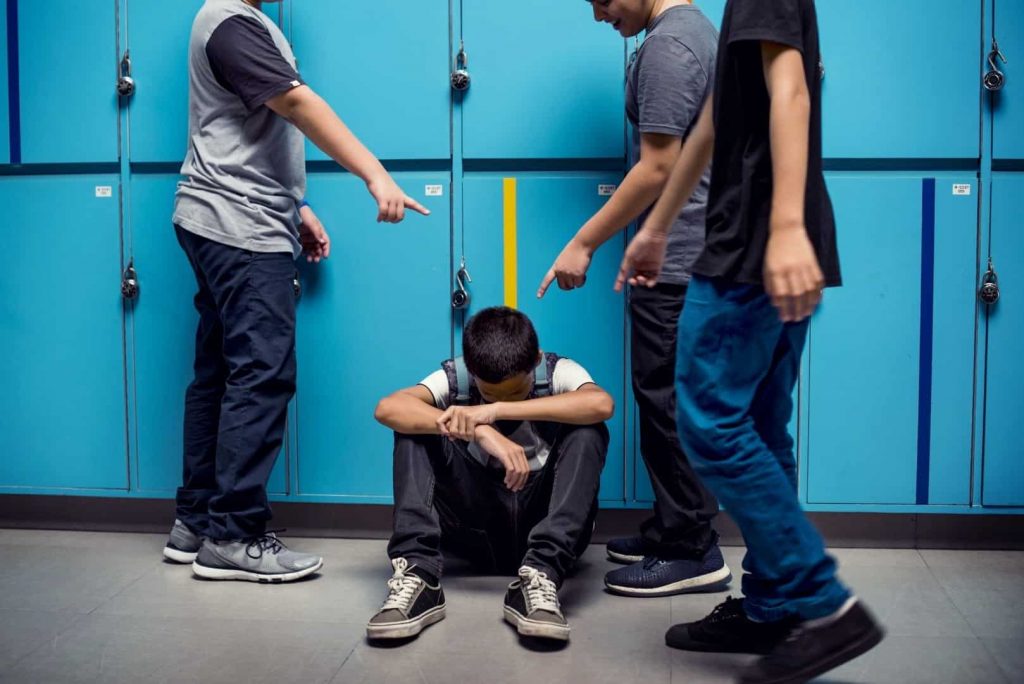 Three older boys pointing on the younger boy, sitting on the floor and hiding his face